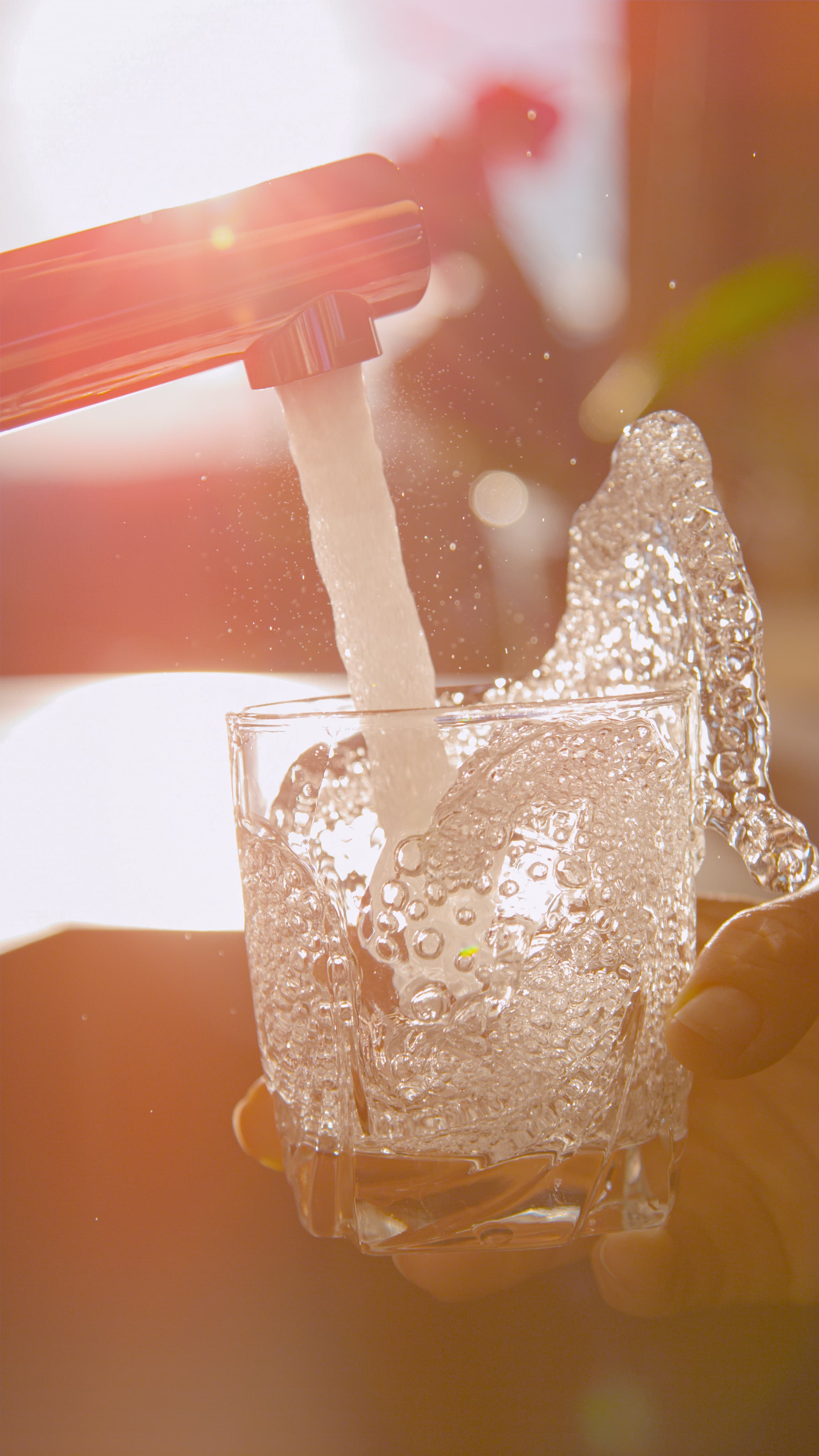 Backlit tap water pouring into a drinking glass in morning sunlight