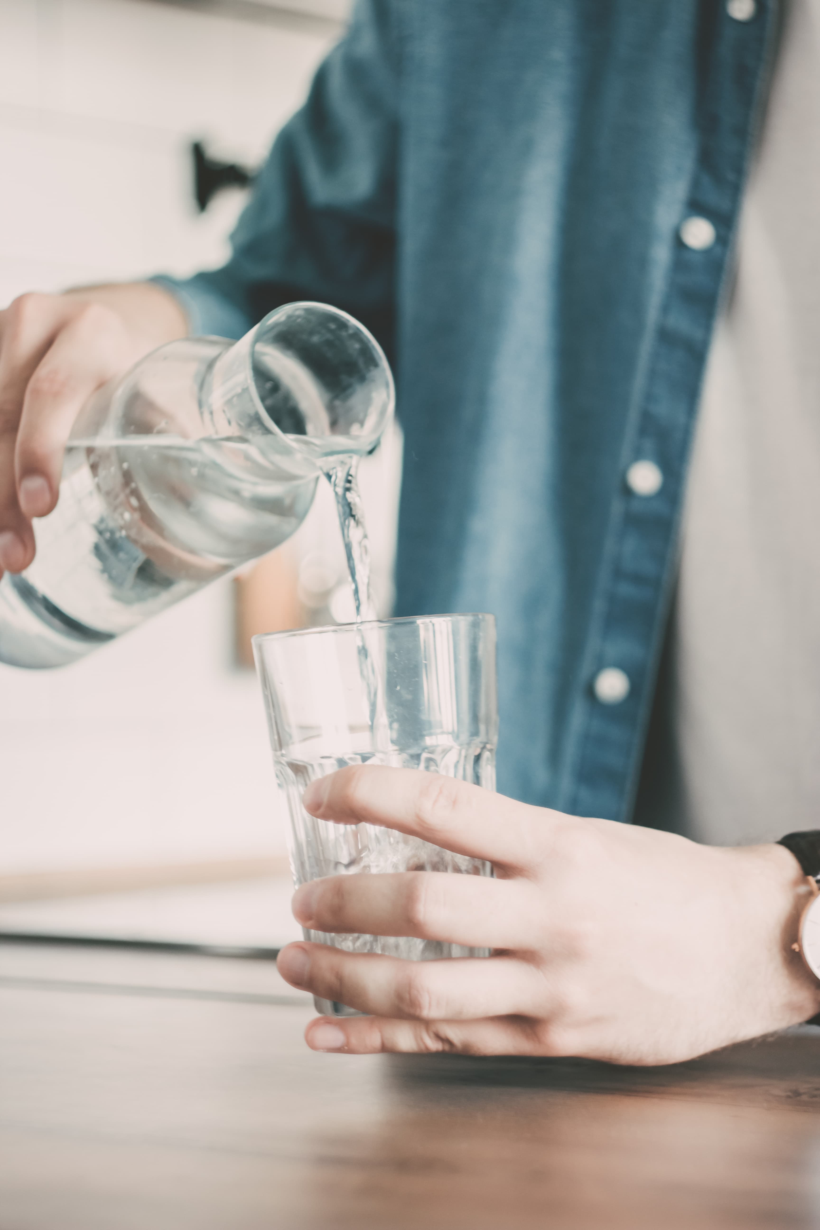 Man pouring a glass of clean filtered water from a carafe at the kitchen table