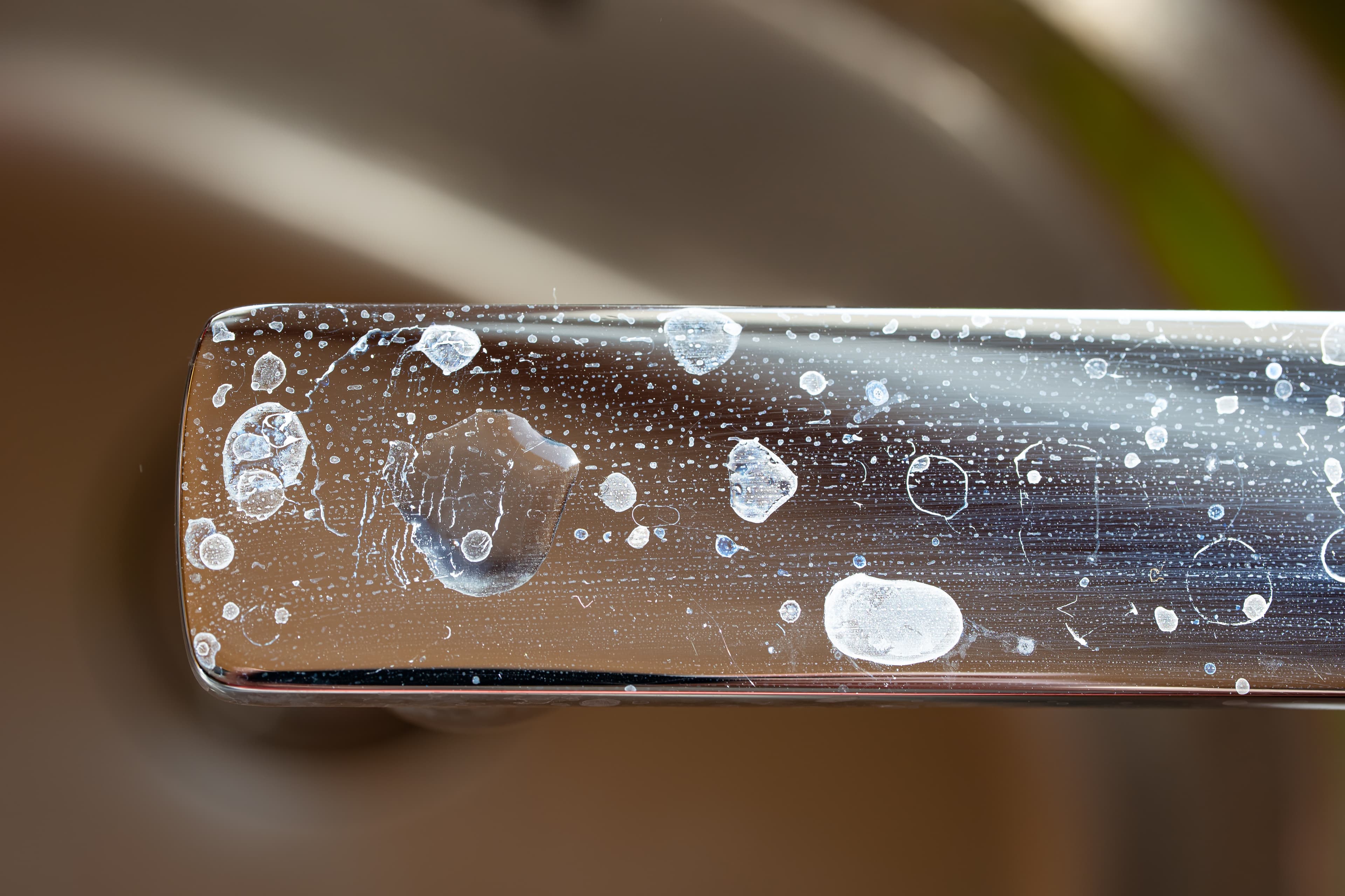 Close-up of white limescale spots and hard-water residue on a chrome faucet handle