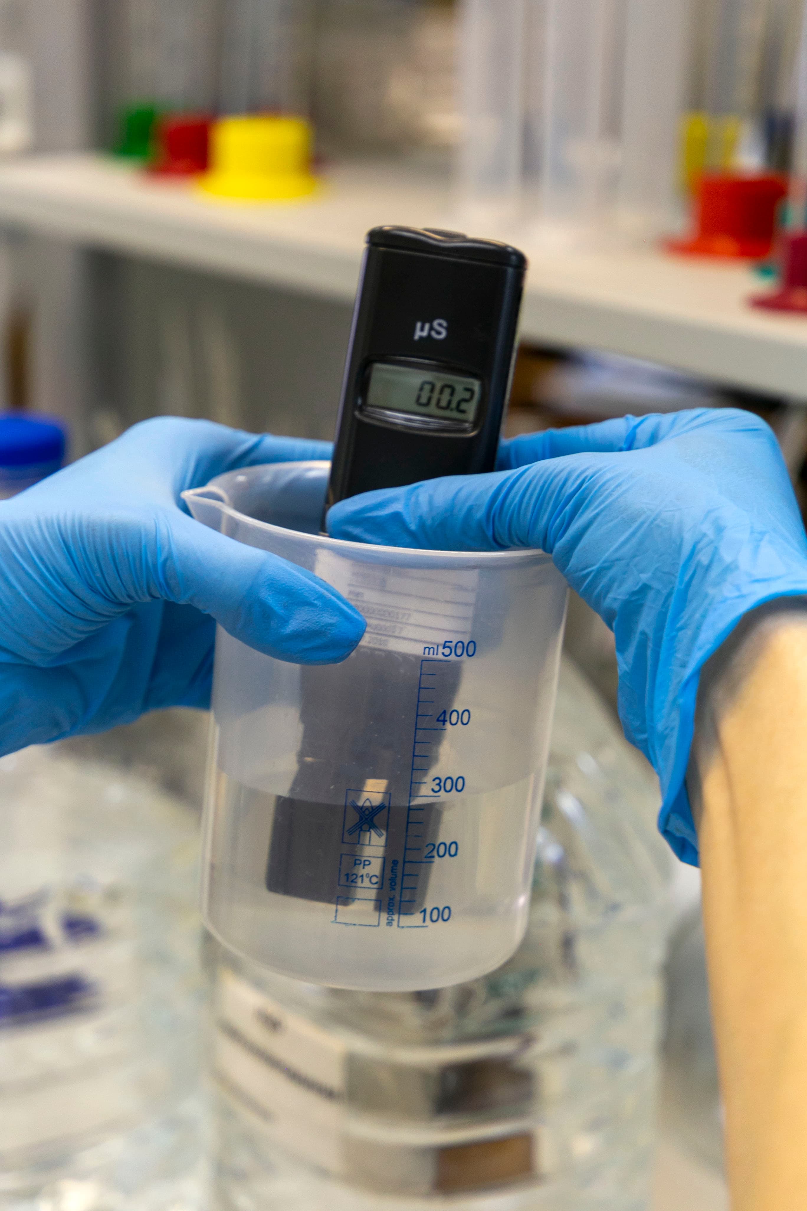 Water testing technician measuring a sample in a glass vial with blue-gloved hands